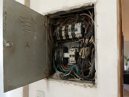 Quadro de luz antigo, com fios emaranhados, fita isolante e disjuntores sem identificação