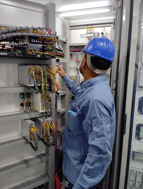 Eletricista de uniforme azul testando um quadro de energia com medidor