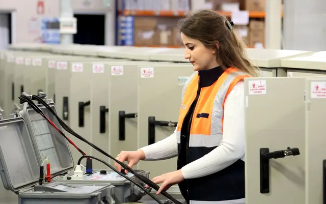 Eletricista de colete laranja operando um painel de energia