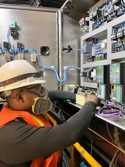 Eletricista de capacete e máscara trabalhando em um quadro de disjuntores