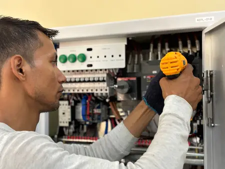 Eletricista com furadeira montando disjuntores em um quadro de distribuição