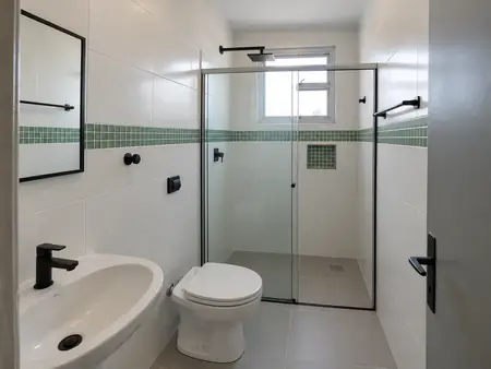Banheiro reformado com porcelanato cinza, revestimento branco, pastilha verde e box de vidro