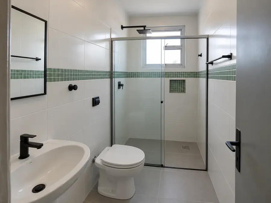 Banheiro reformado com porcelanato cinza, revestimento branco, pastilha verde e box de vidro