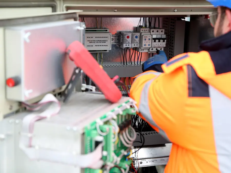Dois eletricistas de colete laranja trabalhando em um painel elétrico
