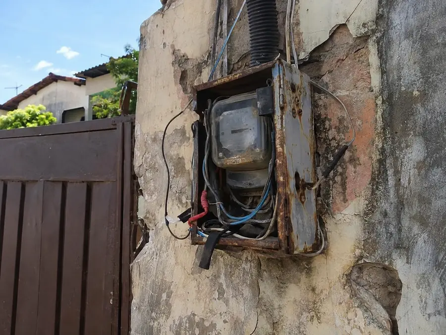 Caixa de medidor enferrujada, com fios soltos na parede externa