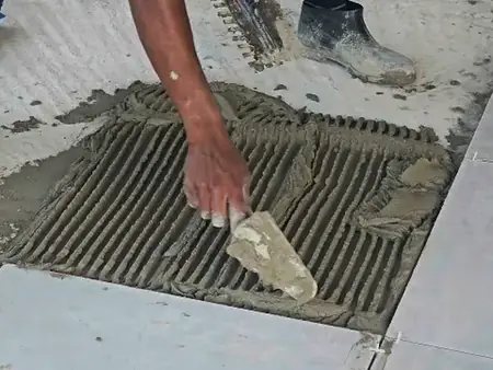 Mãos assentando uma placa grande de porcelanato sobre argamassa com desempenadeira