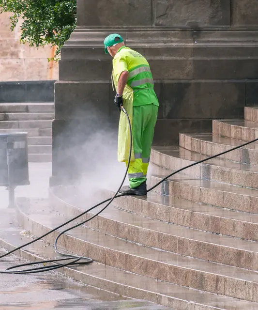 Profissional de uniforme verde lavando uma escada de pedra com jato de água