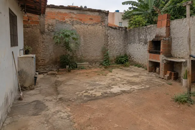 Quintal de terra e cimento irregular com churrasqueira improvisada de tijolos, antes da reforma