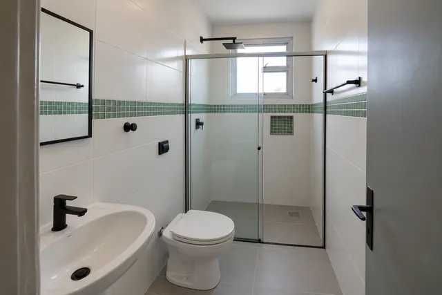 O mesmo banheiro depois da reforma, com porcelanato cinza, revestimento branco, pastilha verde e box de vidro