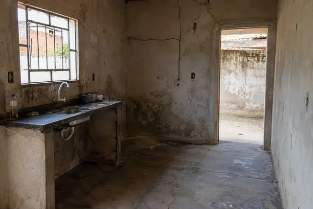 Cozinha com piso de cimento queimado quebrado e paredes só com reboco, antes da reforma